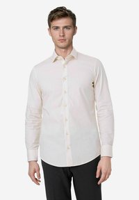 Lichtbeige langemouwen shirt met een spitse kraag, knoopsluiting aan de voorkant en een gladde textuur. De stof is licht getailleerd en heeft een knoopmanchetten.