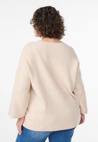 Béžový rebrovaný sveter s voľným strihom, širokými rukávmi a okrúhlym výstrihom, v kombinácii s modrými rifľami. Jemná textúra a ležérny dizajn.