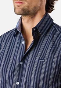 Marine gestreept shirt met verticale strepen in verschillende breedtes, button-down kraag en een linkerkant borstzak met "SEASIDE" borduursel.
