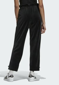 Svarta velourbyxor med elastisk midja, löst sittande och justerbara muddar. Matchas med vita sneakers och ribbade strumpor.