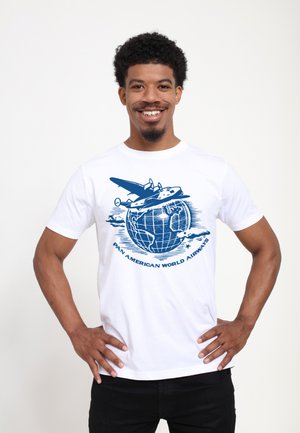 Hvid bomulds T-shirt med et blåt grafisk motiv af et fly over en globe med skyer, mærket "PAN AMERICAN WORLD AIRWAYS."