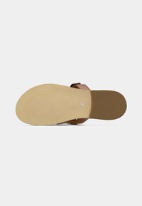 Καφέ σανδάλι με επίπεδη σόλα, σε υφή μπεζ χρώματος. Διαθέτει μία μόνο στραπ για το δάκτυλο του ποδιού και λεπτομέρεια με πόρπη στο πλάι.