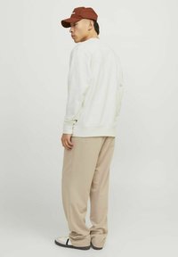 Felpa bianca con maniche lunghe, pantaloni beige e un cappellino marrone. L'outfit presenta una vestibilità rilassata e un design minimalista.