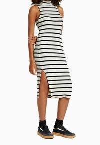 Robe en tricot à col montant, rayures horizontales noires et blanches, fente sur le côté, associée à des baskets noires et des chaussettes noires à mi-mollet.