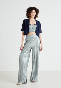 Ljust grönrandig satin crop top och vida byxor i set, kompletterat med en genomskinlig marinblå överdel. Slät textur och mjuk lyster.