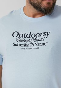 Lichtblauw katoenen t-shirt met korte mouwen, met zwarte tekst: "Buitengevoelens Vooruit! Abonneer Op Natuur®" en "WORD LID VAN S.OLIVER & VRIENDEN."