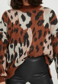 Oversized sweater in a mixed brown, beige, and black leopard pattern. Knitted texture with a ribbed neckline and side slits.