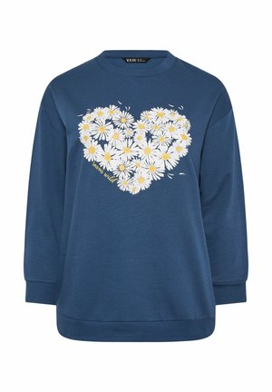 Sininen collegepaita, jossa valkoiset päivänkakkarakukat muodostavat sydämen muodon ja keltaiset "learn wild" -tekstit edessä, pitkät hihat, pyöreä pääntie.