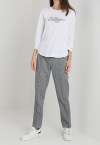 Maglietta bianca a maniche lunghe con grafica "Hilfiger" in colore contrastante; pantaloni felpati grigi a gamba stretta; sneakers bianche con accenti neri.