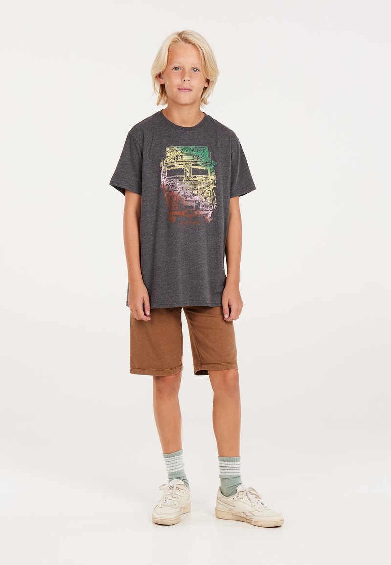 Graues Baumwoll-T-Shirt mit buntem Grafikdruck, kombiniert mit braunen Shorts. Das Model trägt weiße Sneaker und grün gestreifte Socken.