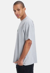 Gray cotton t-shirt with short sleeves, round neck, and relaxed fit. Features a small graphic on the chest. Smooth texture.
