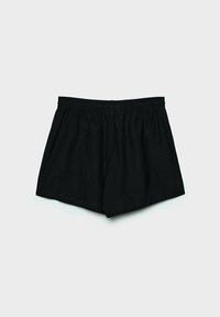 Mustat elastiset vyötäröshortsit, asetettuna tasaisesti vaaleanharmaata taustaa vasten.