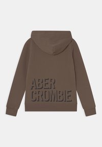 Felpa marrone con tasca a marsupio anteriore, cappuccio e grande testo nero "ABERCROMBIE" stampato sul retro. Realizzata in tessuto morbido.