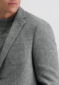 Grijze, gestructureerde blazer met een houndstoothpatroon, voorzien van een notch lapel, een enkele borstzak en een subtiele metalen acccent op de kraag.
