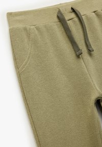 Oliwkowe dresy z dzianiny z rypsowym pasem, detalem ze sznurkiem i dwoma bocznymi kieszeniami, wyróżniające się fakturowanym wykończeniem tkaniny.