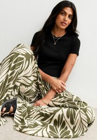 Black fitted t-shirt paired with a flowy, cream and olive green patterned maxi skirt featuring large leaf prints and a relaxed fit.