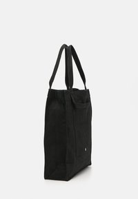 Black canvas tote bag with long handles, rectangular shape, exterior pocket, and subtle logo detail on the bottom. Smooth texture.