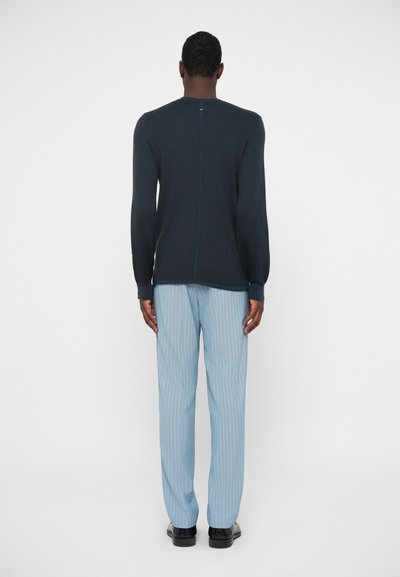 Marineblaue, gerippte Langarm-Strickjacke mit Rundhalsausschnitt, kombiniert mit hellblauen gestreiften Hosen und schwarzen Schuhen, von hinten betrachtet.