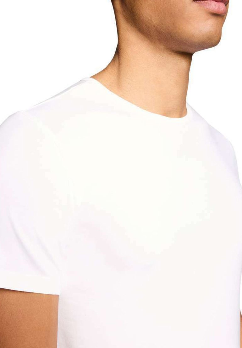 Gros plan sur une personne portant un t-shirt blanc uni à manches courtes et col rond, montrant le cou, l'épaule et une partie du visage.