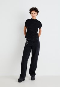 Svart t-shirt med korta ärmar, kombinerad med högmidjade svarta jeans. Noterbar nyckelring som är fäst vid byxorna.