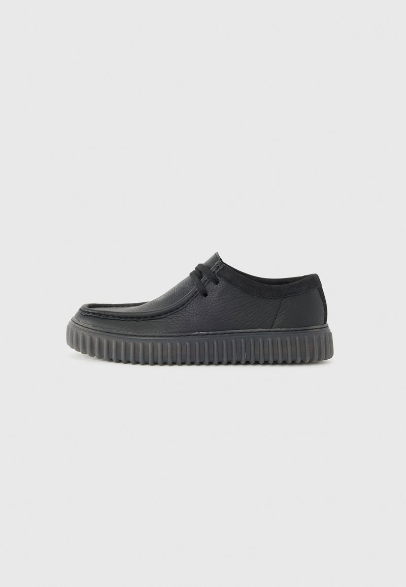 Black leather casual shoes with a rounded toe, low profile, and thick ridged rubber sole. Features a lace detail and smooth texture.