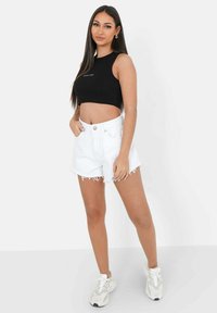 Top corto negro con texto blanco, combinado con pantalones cortos de mezclilla blanca de cintura alta con dobladillos deshilachados y zapatillas de colores claros.