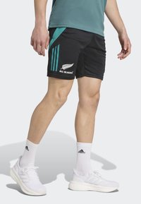Black athletic shorts with teal accents, featuring three vertical stripes and "ALL BLACKS" text, paired with white sneakers and socks.