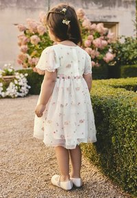 Weißes Kleid mit Blumenstickerei, kurzen Puffärmeln und einem rosa Band in der Taille. Das Kleid verfügt über einen Knopfverschluss auf der Rückseite.