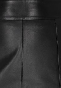 Primo piano di un tessuto in pelle nera con cuciture e texture visibili, che mostra pannelli di superficie lisci e leggermente rugosi.