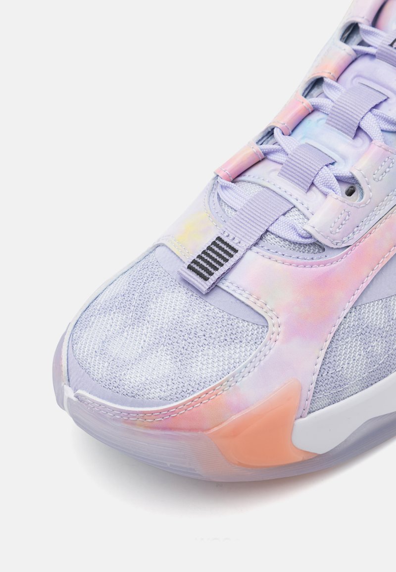 Primer plano de la punta de una zapatilla morada con tela de malla, acentos en naranja pastel y rosa, y una correa lavanda sobre los cordones morados claros.