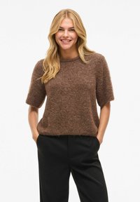 Brun, myk kortermet genser med rund hals, kombinert med svarte bukser. Teksturen ser myk og behagelig ut.