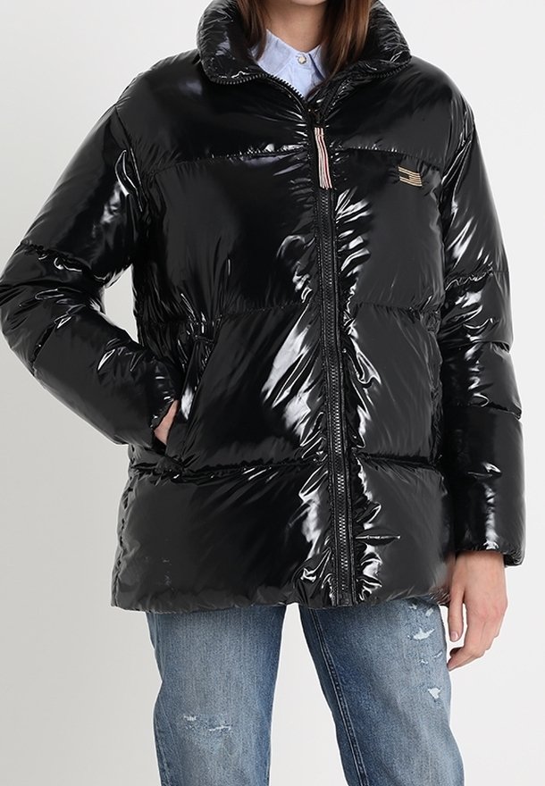 Černá péřová bunda s lesklým povrchem, zipem v přední části, vysokým límcem a nášivkou na hrudi; doplněná o roztrhané modré džíny.
