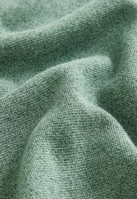 Material tricotat verde, cu o suprafață texturată, prezentând un model moale, ușor stropit, conceput cu o cădere lină și o strălucire subtilă.