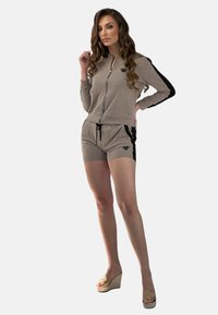 Beżowy zestaw sportowy zawierający kurtkę zapinaną na zamek z logo serca oraz pasujące szorty z czarnymi akcentami bocznymi, wykonany z miękkiego materiału.