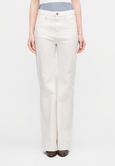 Άσπρο, ψηλόμεσο παντελόνι με φαρδιά μπατζάκια από βαμβάκι, με μπροστινές τσέπες, ορατά ραφές και κούμπωμα με κουμπί μπροστά, συνδυασμένο με καφέ παπούτσια.