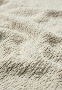 Tissu crème texturé avec un motif épais et tissé. Présente une surface douce et légèrement inégale, ce qui renforce son attrait tactile.