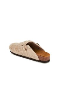 Fuzzy beige slide slipper features a sheepskin upper, cork footbed, and a flat rubber sole, with two side buttons and open back design.