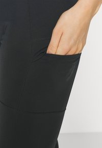 Svarta leggings i stretchmaterial med en sidaficka. Har platta sömmar och en jämn yta. Figursydd design.