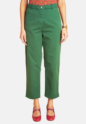 Grüne Baumwollhose mit geradem Bein, ausgestattet mit einem vorderen Knopfverschluss und dezenten Taschenakzenten. Kombiniert mit leuchtend roten Schuhen.