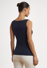 Top de alças ajustado azul-marinho com decote redondo e alças largas, feito de um tecido liso e elástico, combinado com calças de cor clara.