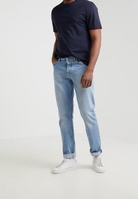 Jasnoniebieskie dżinsy o prostym kroju z podwiniętymi mankietami, w połączeniu z granatową koszulą i białymi sneakersami. Gładka faktura, casualowy design.