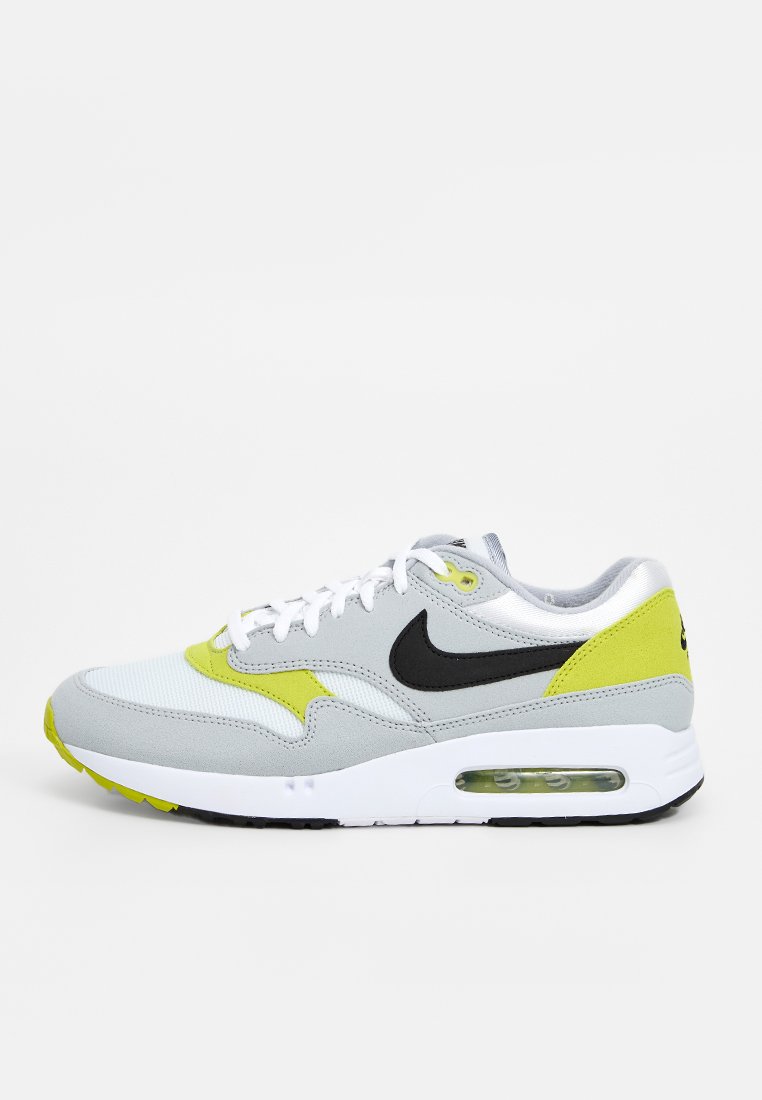 Nike Air Max 1 sneaker, met een bovenwerk van grijs suede en mesh, zwart logo en heldere gele accenten. Witte zool met zichtbare luchtunit.