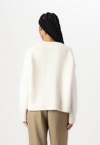Kremfarget, oversized strikkegenser med ribbestrikkede mansjetter og hem. Myk tekstur og litt boksformet fasong. Brukt med beige bukser.