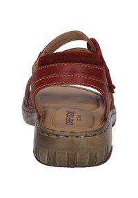 Rote Wildleder-Riemchensandale mit einer gepolsterten braunen Innensohle, leichter Sohle und gebogenem Absatz. Auffällige Nähte und offene Seiten.