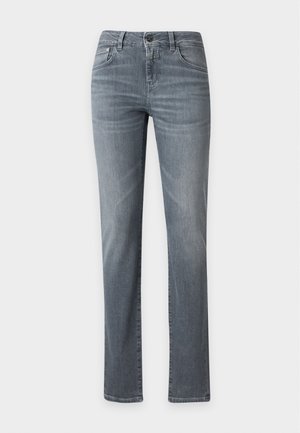 Personne debout portant une chemise à carreaux verte et noire boutonnée, un jean bleu délavé et des chaussures à lacets rouge foncé avec des lacets blancs.