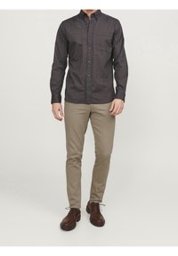 Chemise à rayures foncées à boutons bleus, associée à un pantalon chino beige clair et des chaussures en cuir marron. La chemise est dotée d'un col et d'une poche poitrine.