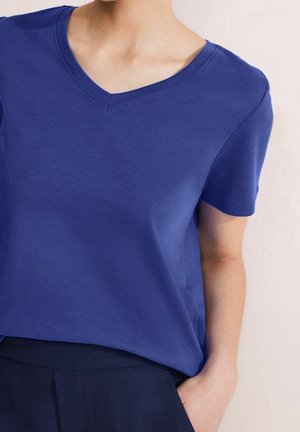 Lilla T-shirt med korte ærmer og V-hals, lavet af blød bomuld, med en afslappet pasform og glat tekstur, kombineret med mørkfarvede bukser.