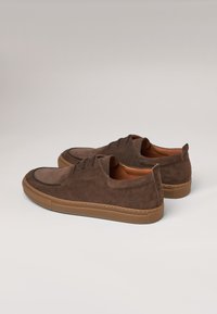 Chaussures en suede marron avec un bout arrondi, un design à lacets et une semelle en caoutchouc avec une couleur contrastante beige sur le dessous.
