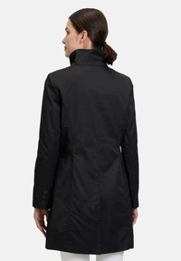 Sort trenchcoat med høj krave, knappede ærmer og skræddersyet pasform. Har en glat, mat tekstur og detaljering med bagsømme.