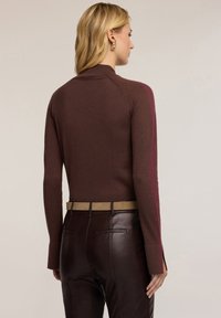 Brązowy dopasowany sweter z długimi rękawami, kontrastowymi bordowymi panelami bocznymi, ściągaczami na rękawach oraz prostym dołem, w zestawie z eleganckimi brązowymi skórzanymi spodniami.